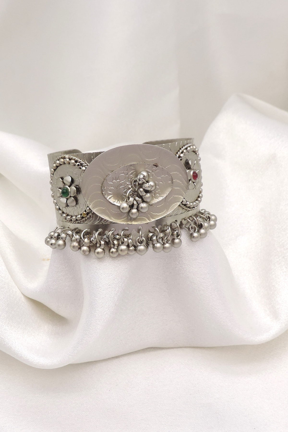 Oxidized silver floral ghungroo cuff bracelet with engraved detailing, colorful stone accents, and dangling silver charms by joyrias