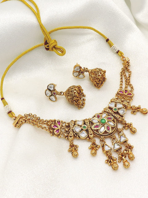 Antique gold-tone kundan choker necklace set with matching jhumka earrings featuring ruby and emerald-inspired accents, ideal for bridal wear, weddings, and festive occasions.