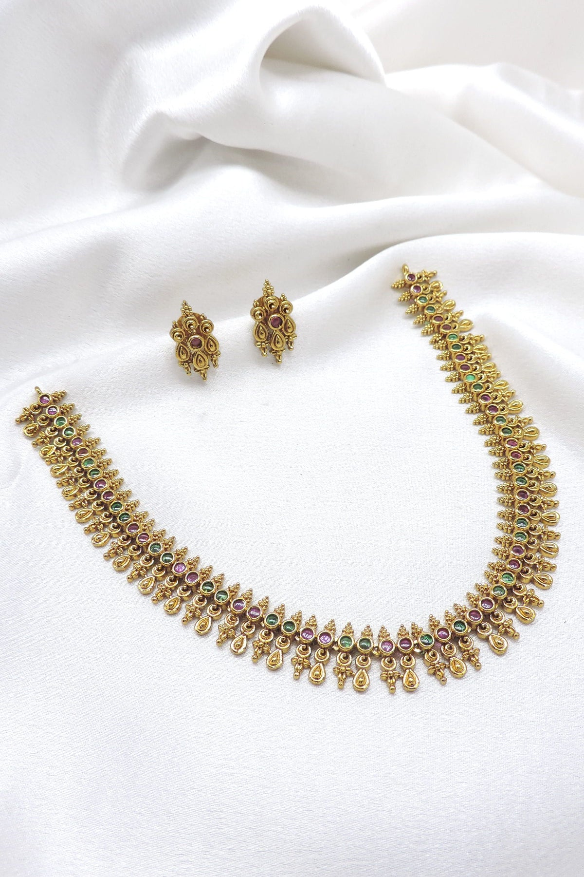 Ruby emerald traditional necklace set with intricate gold-tone motifs and matching stud earrings by joyrias