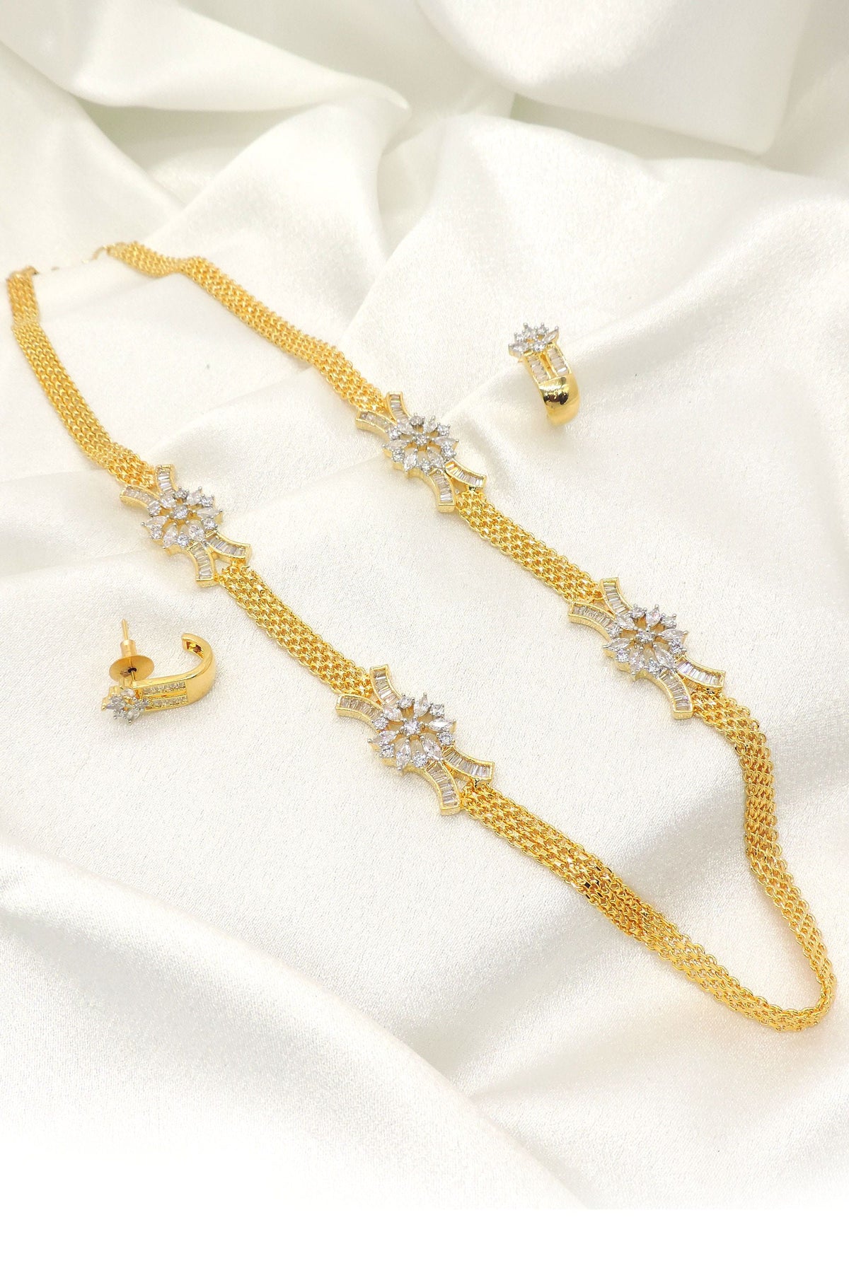 Gold plated floral AD chain necklace set with matching earrings, featuring floral motifs and sparkling AD stones, displayed on satin background.