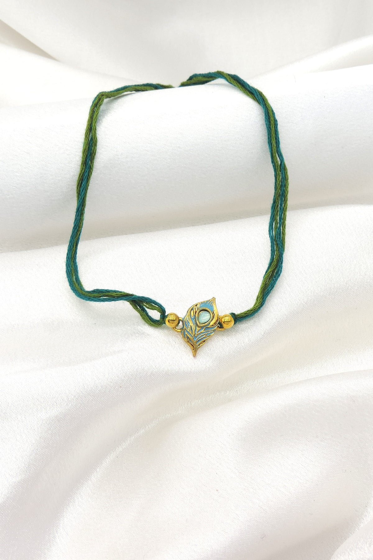 Peacock feather bhaiya rakhi with teal blue enamel and gold detailing by Joyrias