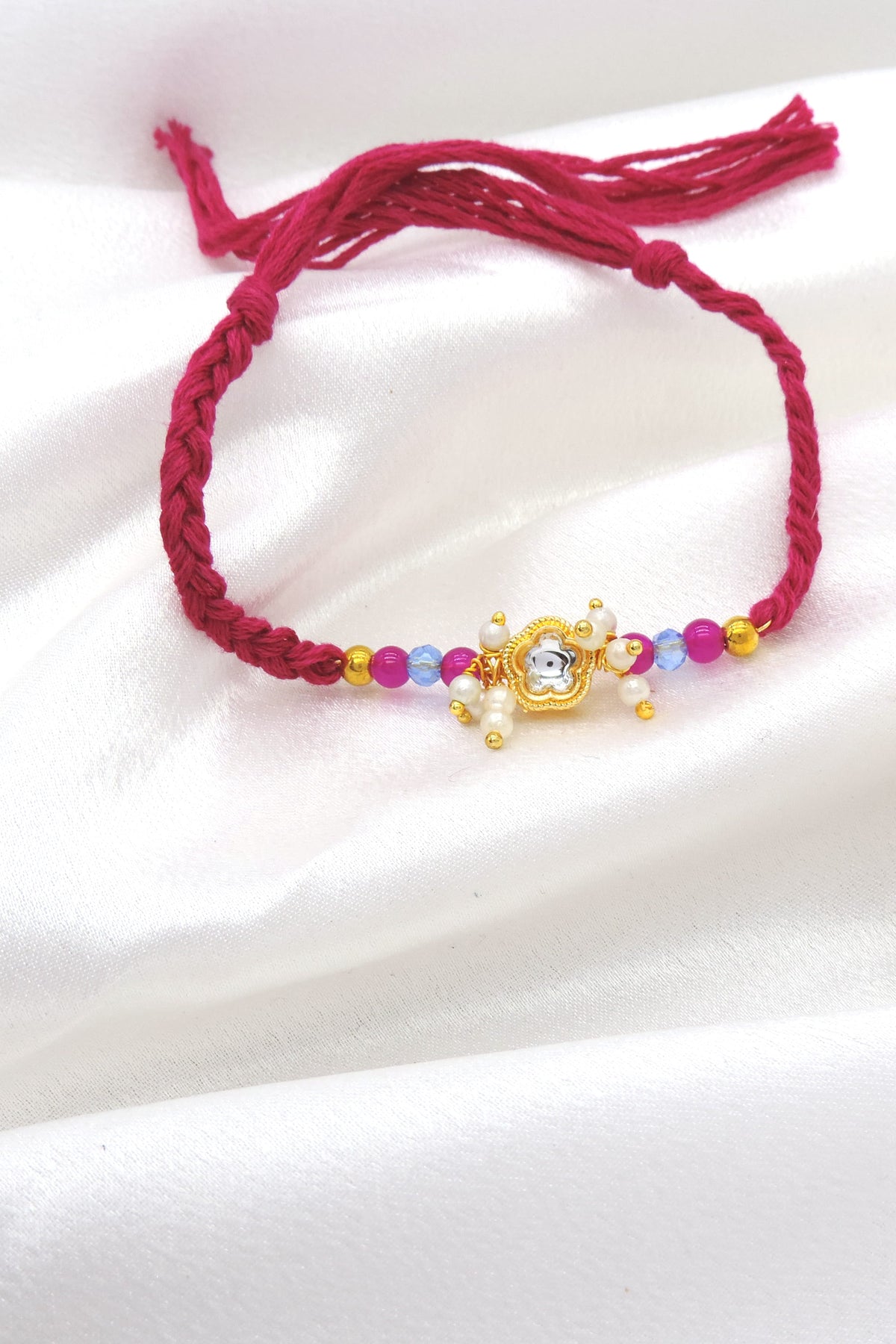 Gold floral pearl cluster bhaiya rakhi with kundan accent and pink blue beads on magenta thread by Joyrias