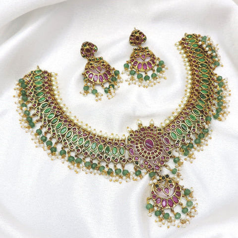 Temple kundan choker necklace set with green and pink stones, pearl detailing and matching earrings by joyrias