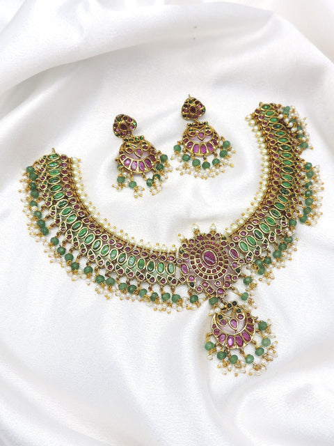 Temple kundan choker necklace set with green and pink stones, pearl detailing and matching earrings by joyrias