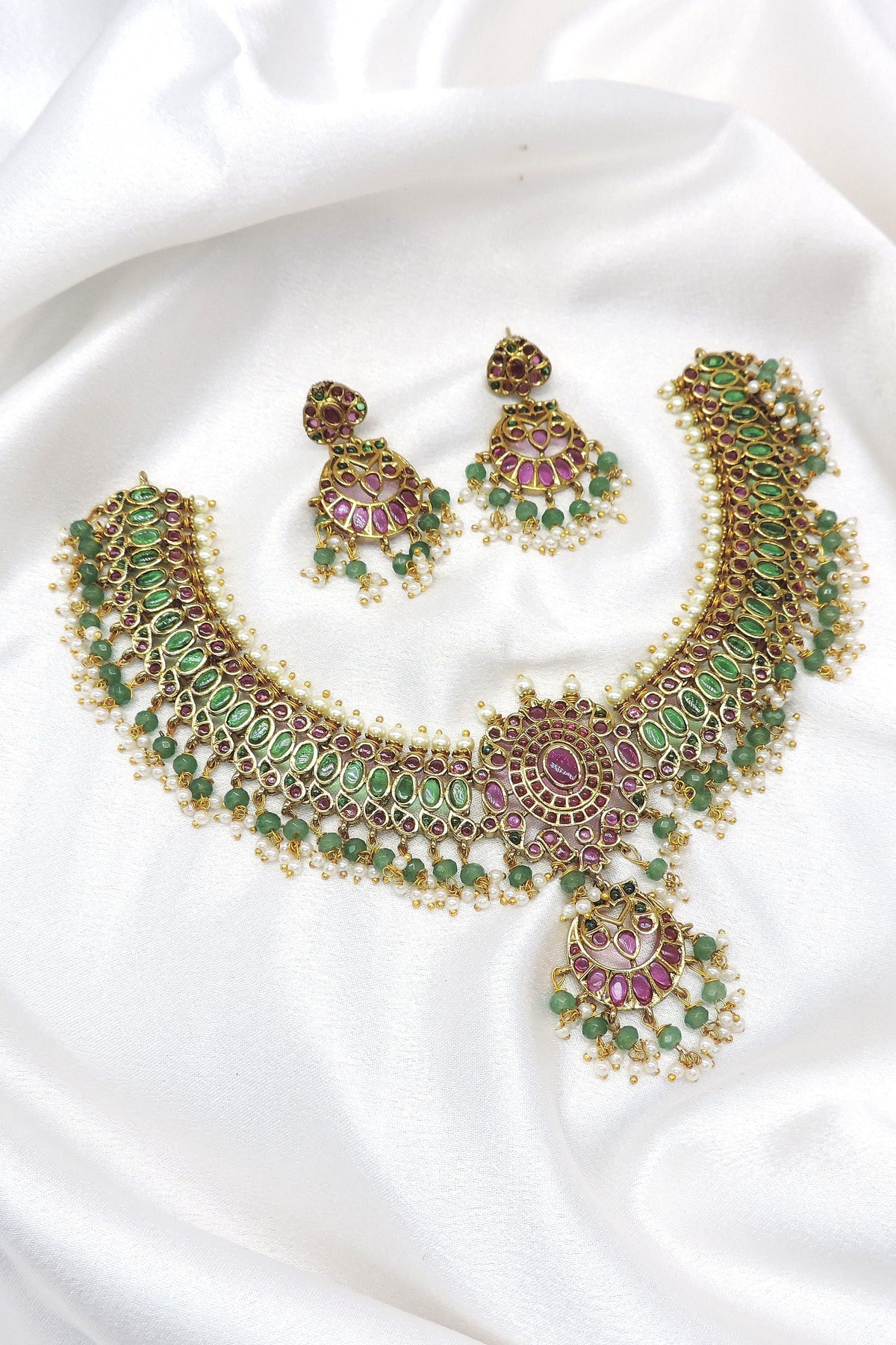 Temple kundan choker necklace set with green and pink stones, pearl detailing and matching earrings by joyrias