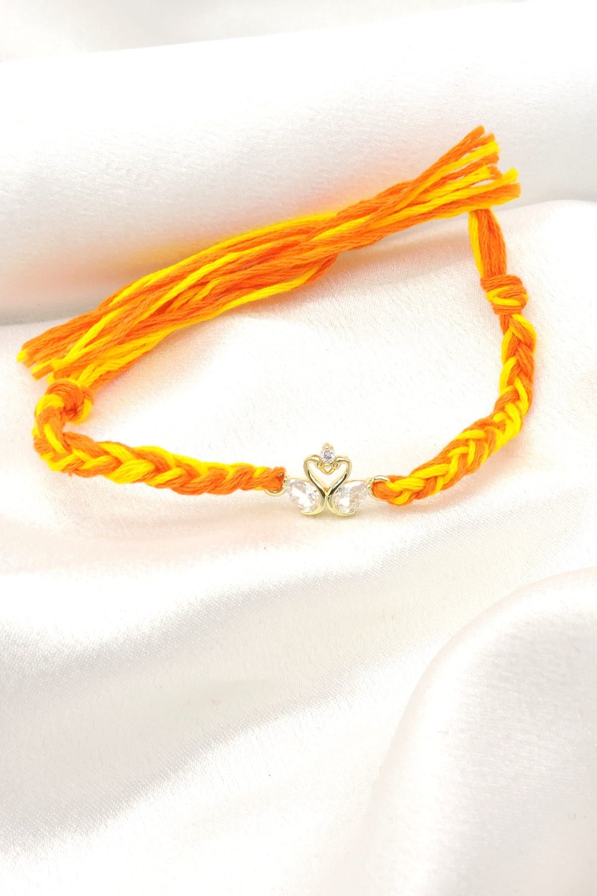 CZ swan bhaiya rakhi with gold swan duo charm and CZ teardrop wings on braided yellow orange thread by Joyrias