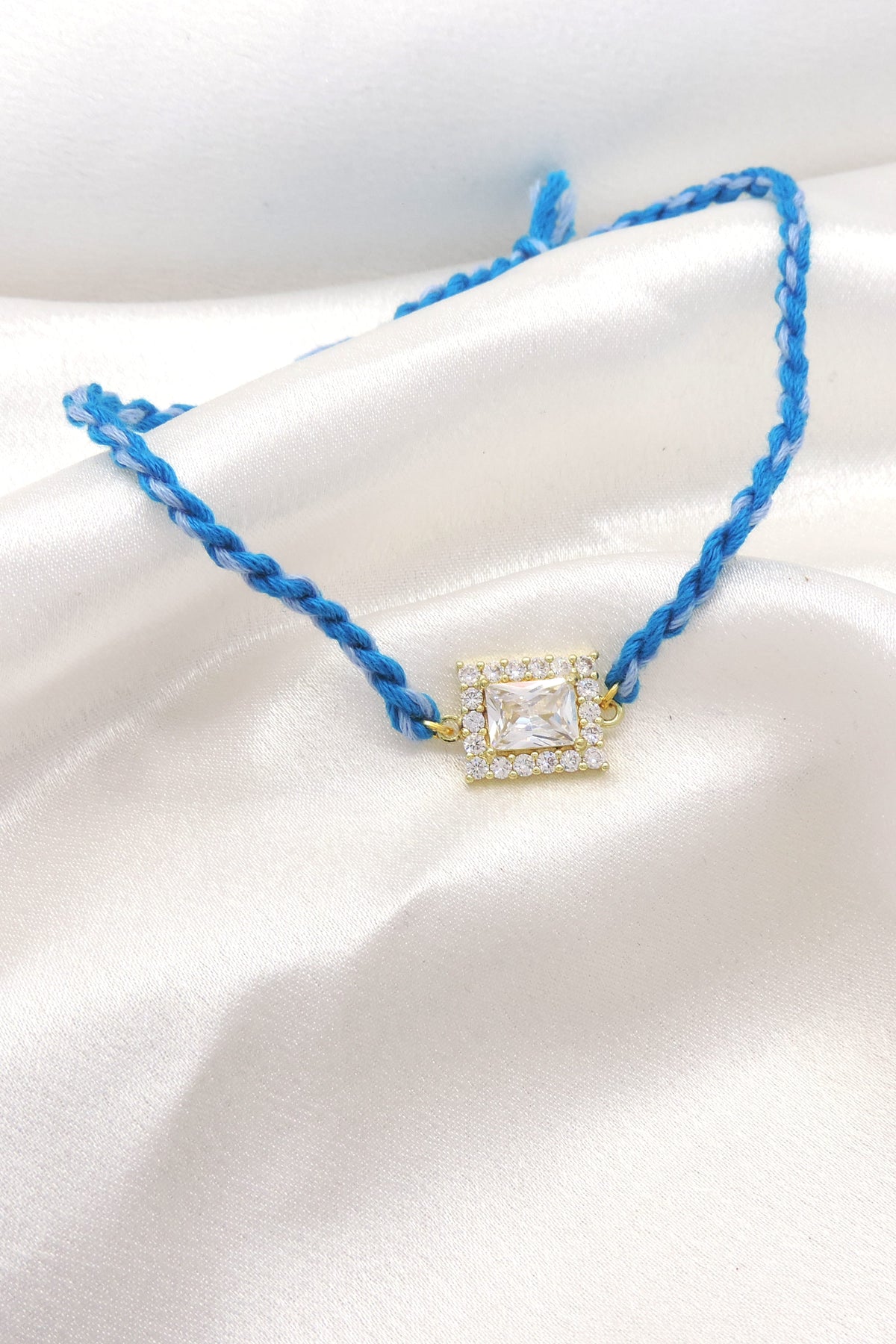 CZ square solitaire bhaiya rakhi with CZ halo border on braided blue thread by Joyrias