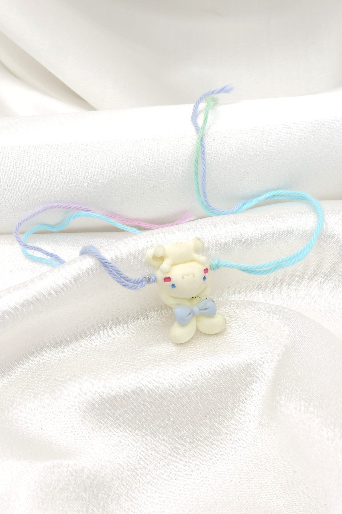 Teddy bear kids rakhi with 3D white bear charm and blue bow on pastel multicolor thread by Joyrias